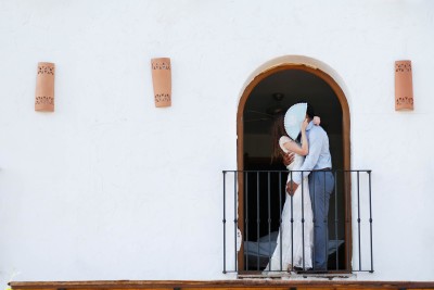 couple hide their kissing behind a fan in a Spanish arch doorway