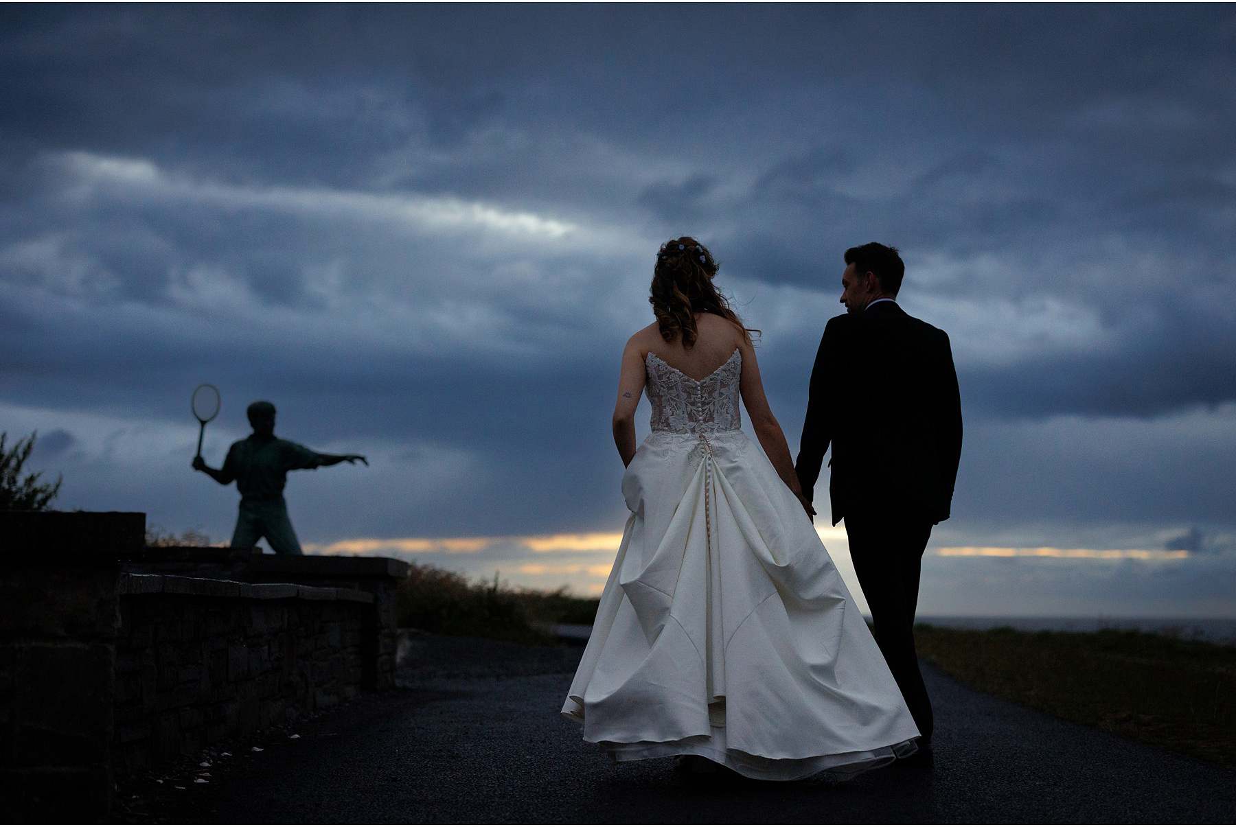 bride and groom walk by the statue of Richard Harris near diamond rocks in Kilkee county clare